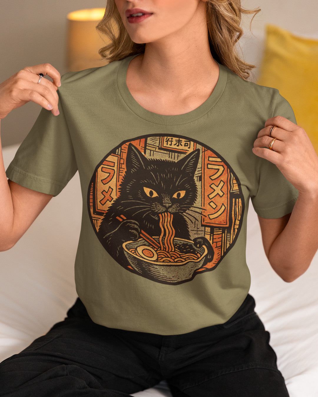 woman earing a green t-shirt with an image of a black cat eating noodles on it.
