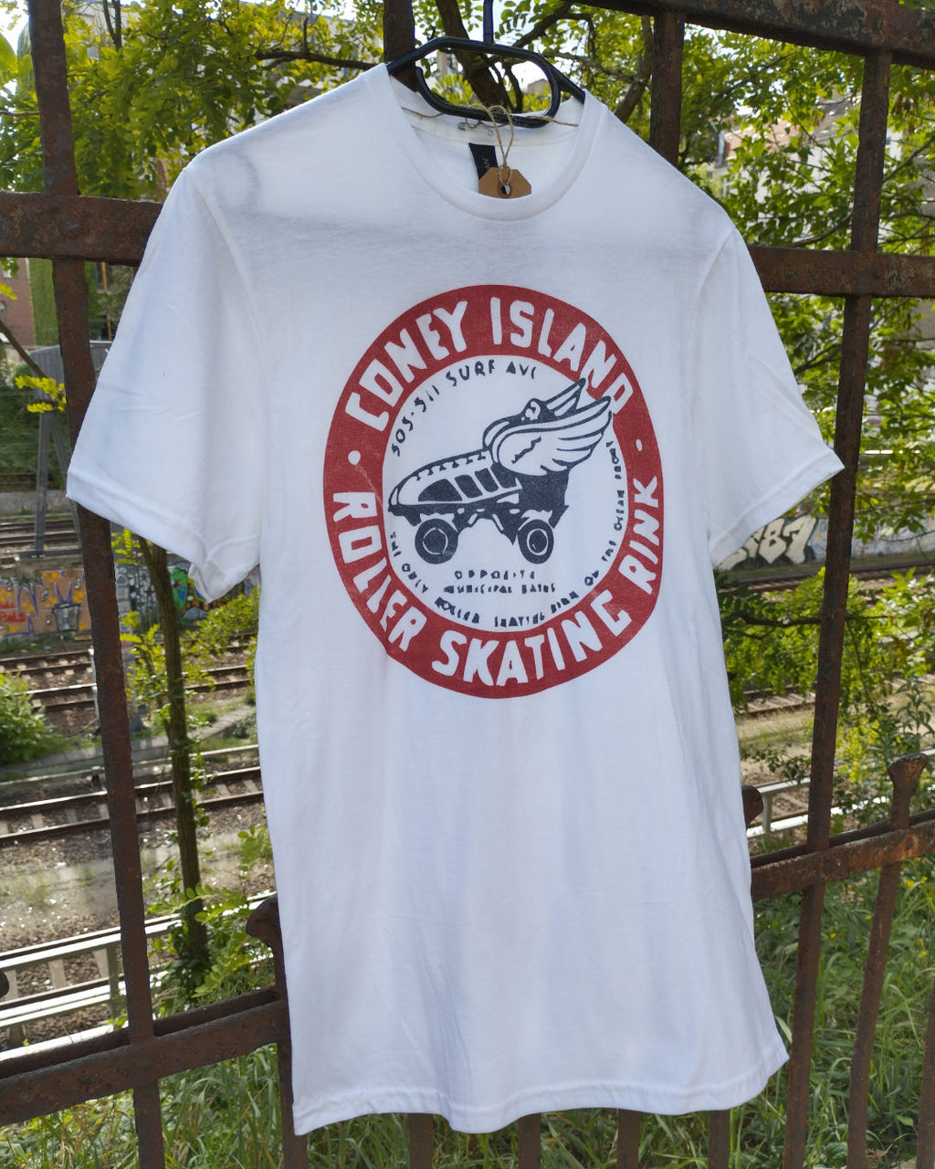 White t-shirt with a red and black graphic design hanging on a rusty metal fence.