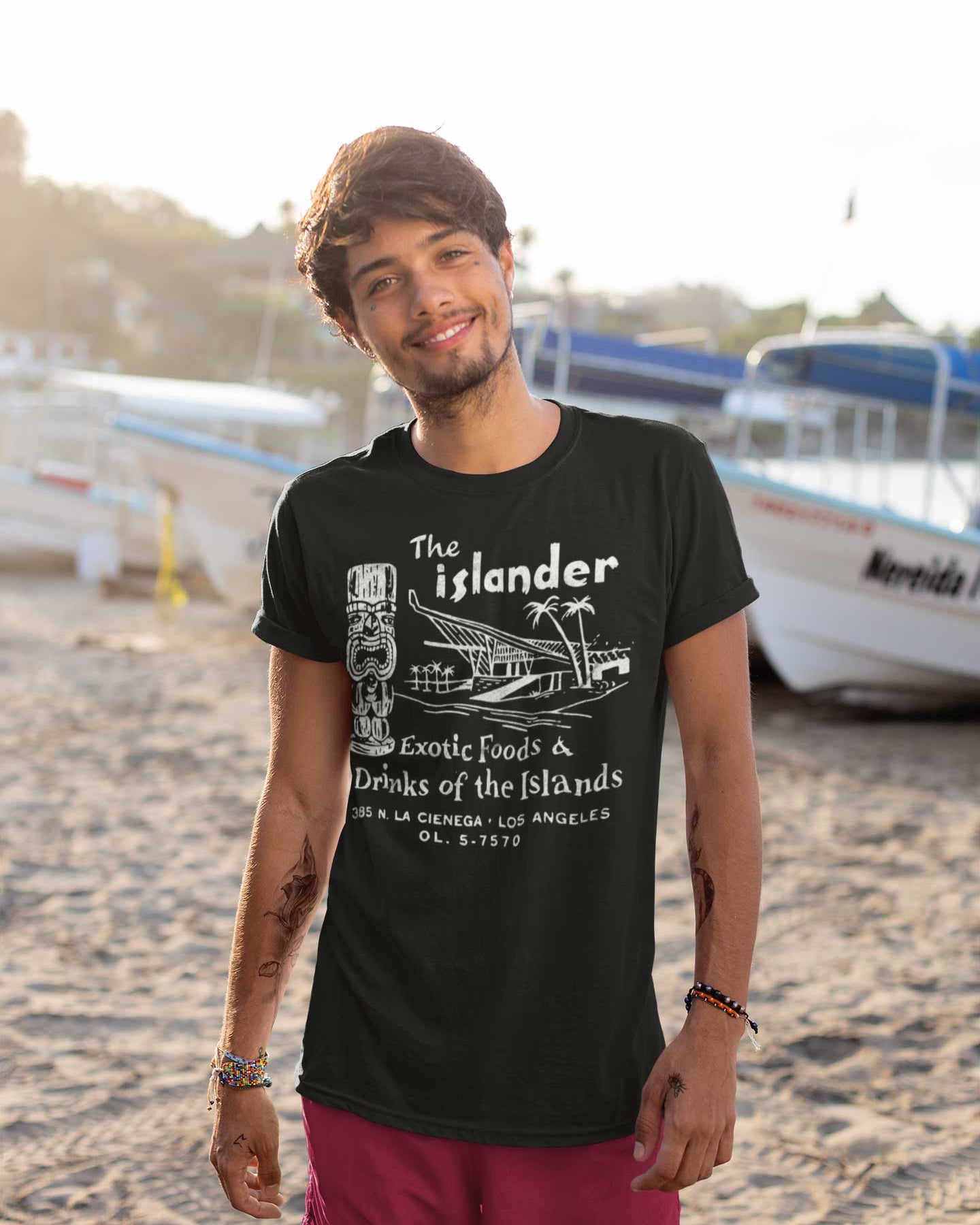 Man wearing a black t-shirt with 'The Islander' design on a beach