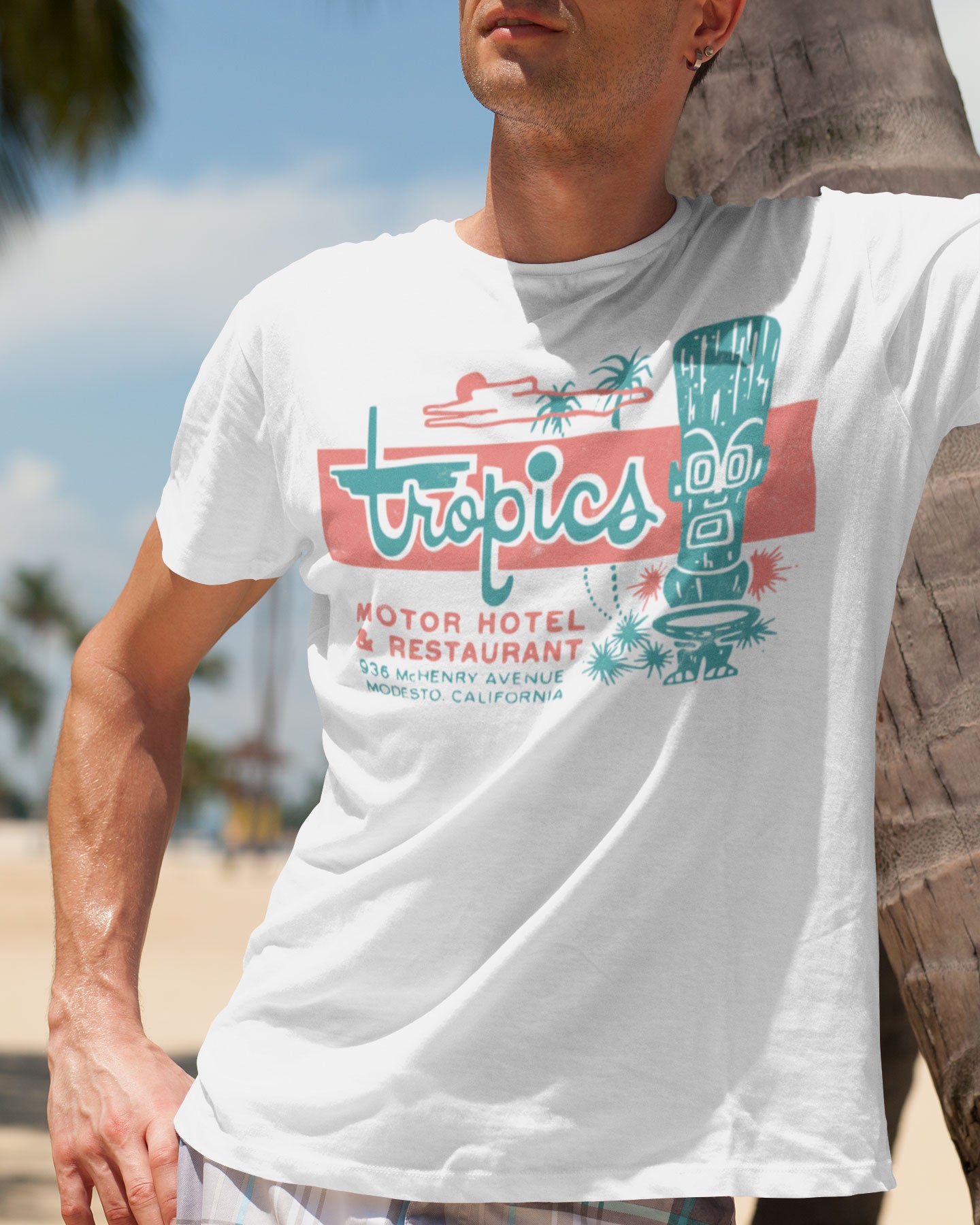 Man wearing a white t-shirt with 'Tropics Motor Hotel & Restaurant' graphic design.