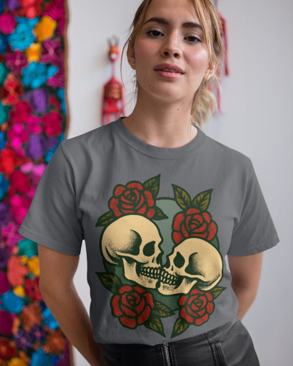 Person wearing a gray t-shirt with a skull and roses design in front of colorful floral decorations.