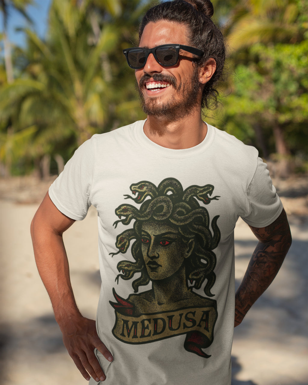 Man wearing a white t-shirt with Medusa graphic and 'MEDUSA' text, standing outdoors with greenery in the background.