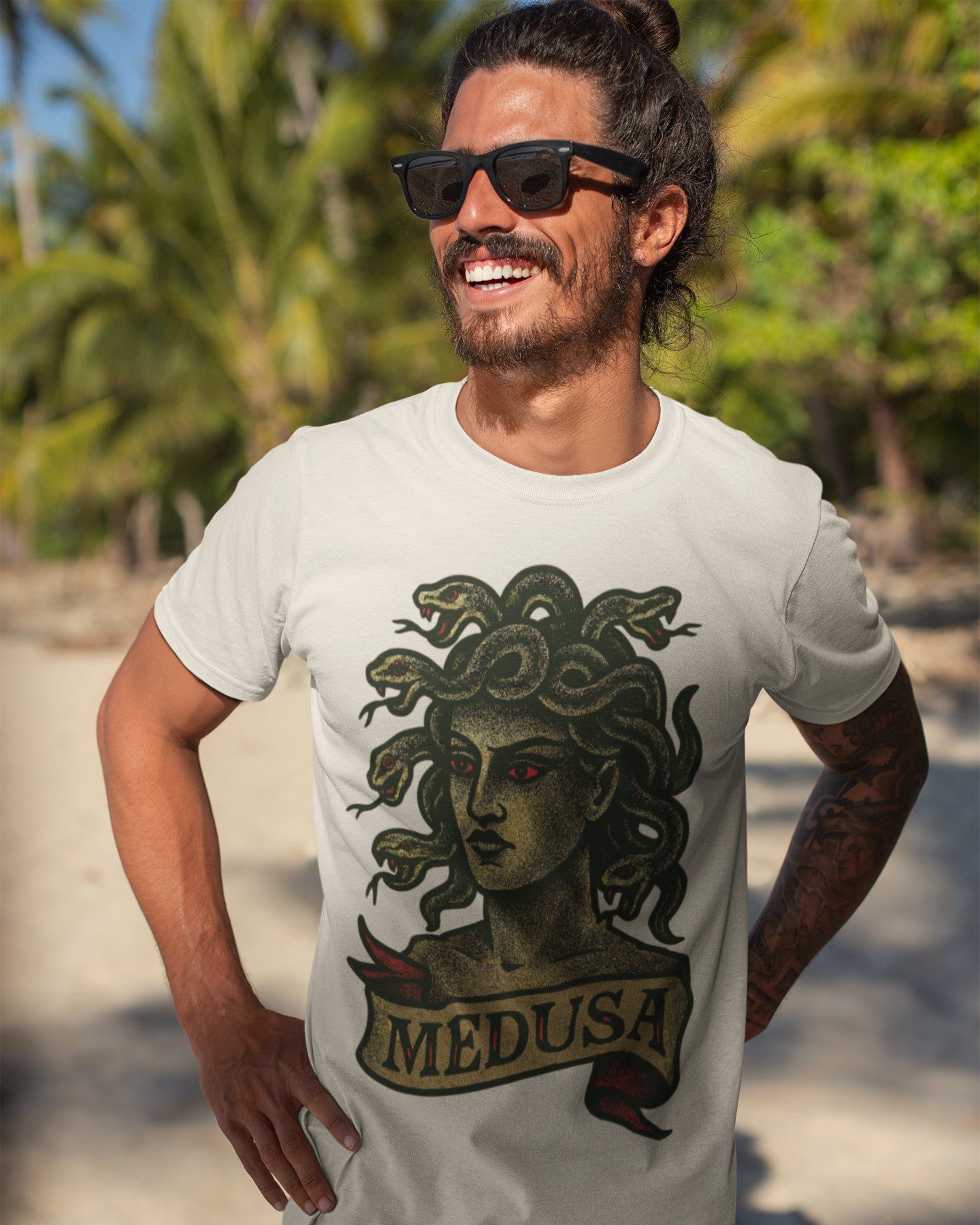 Man wearing a white t-shirt with Medusa graphic and 'MEDUSA' text, standing outdoors with greenery in the background.