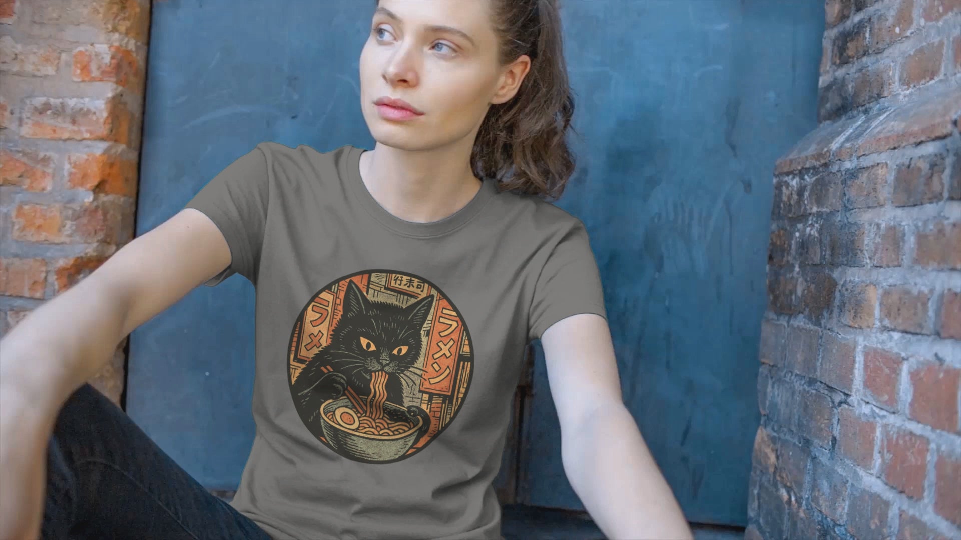 Woman wearing a charcoal T-Shirt depicting a black cat eating ramen noodles
