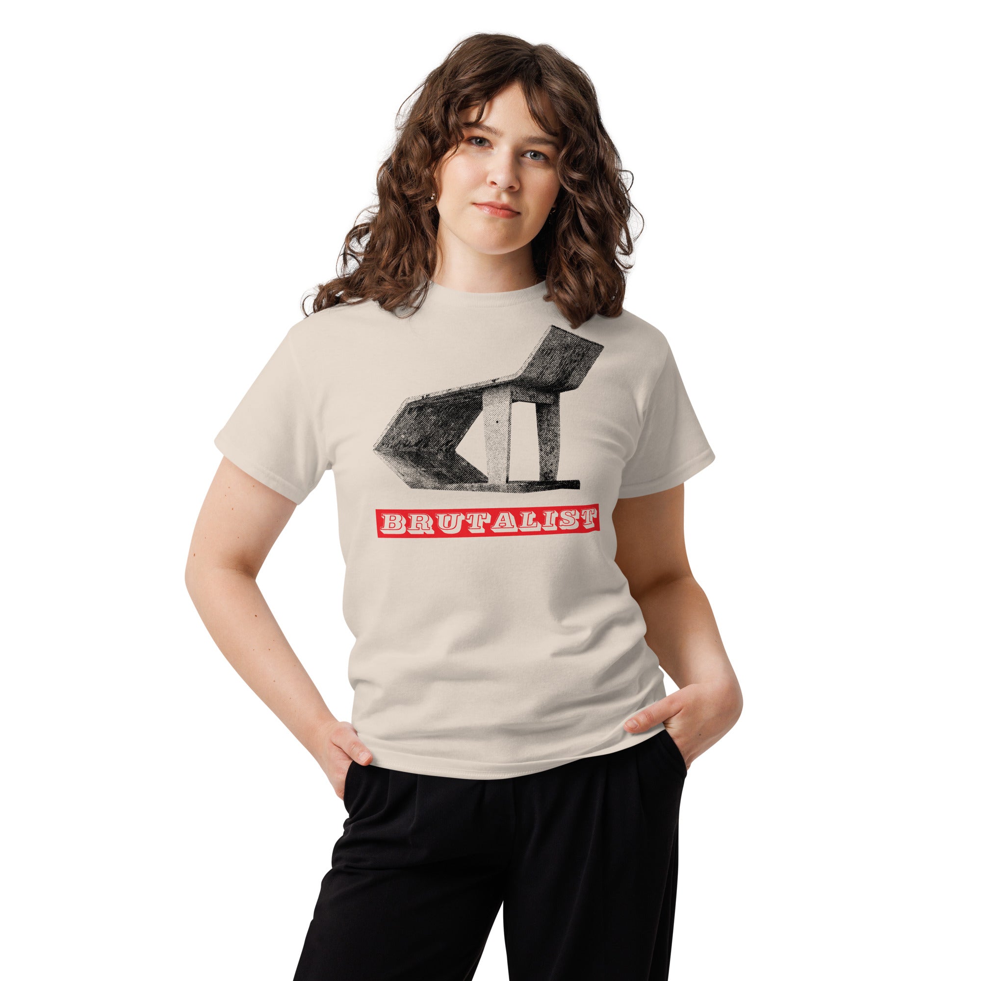 A woman modeling a light beige graphic t-shirt with a soviet bus stop illustration and the word Brutalist in red block letters, paired with black pants against a plain white background.
