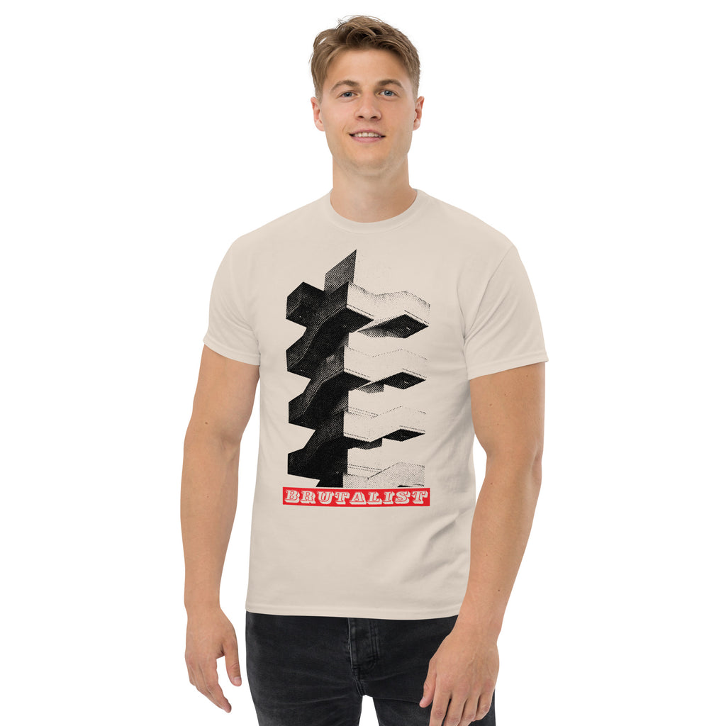 A man wearing a light beige crewneck t-shirt with a black geometric graphic and a red banner reading 'BRUTALIST' on the front, set against a plain white background.
