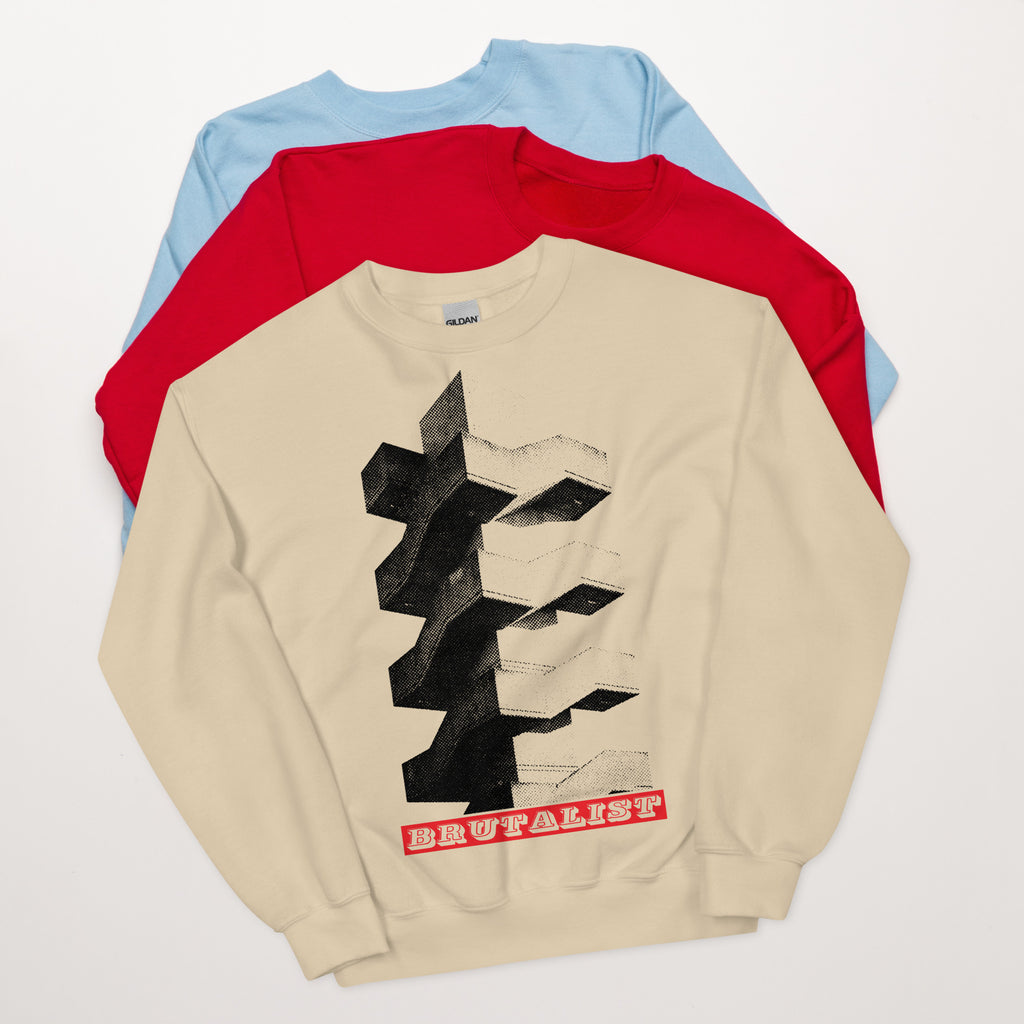 Three crewneck sweatshirts layered in a fan arrangement on a light gray background. The front sweatshirt is beige with a large black geometric graphic and red text reading 'Brutalist'.
